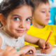 Photo of a girl and a boy at a table in a preschool room