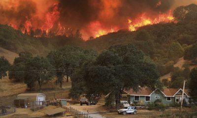 Wildfire burns on hills above rural home.