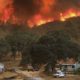 Wildfire burns on hills above rural home.