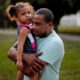 Photo of Jose Perez-Santiago, right, holding his daughter Jordalis, 2, as they return to their home for the first time since it was flooded