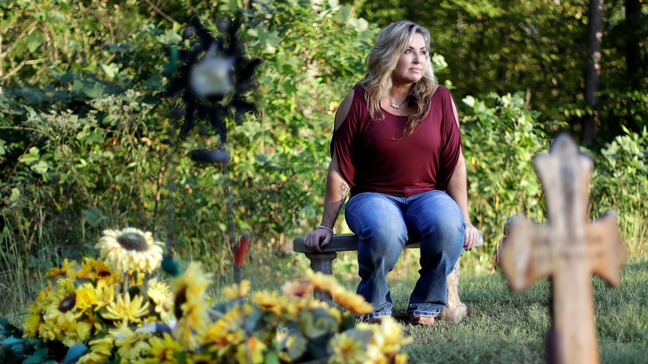 Photo of Heather Melton sitting by the grave of her late husband, Sonny Melton