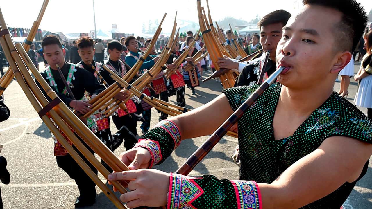 Photo of Phia Chia performing on a traditional Hmong instrument, the qeej