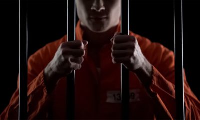 Photo of a man in an orange jumpsuit behind prison bars