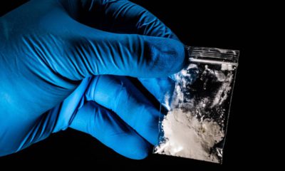 Photo of a gloved hand lifting up a package of powdered fentanyl