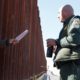 Photo of a journalist sticking her microphone through a through a border fence to interview a Border Patrol agent