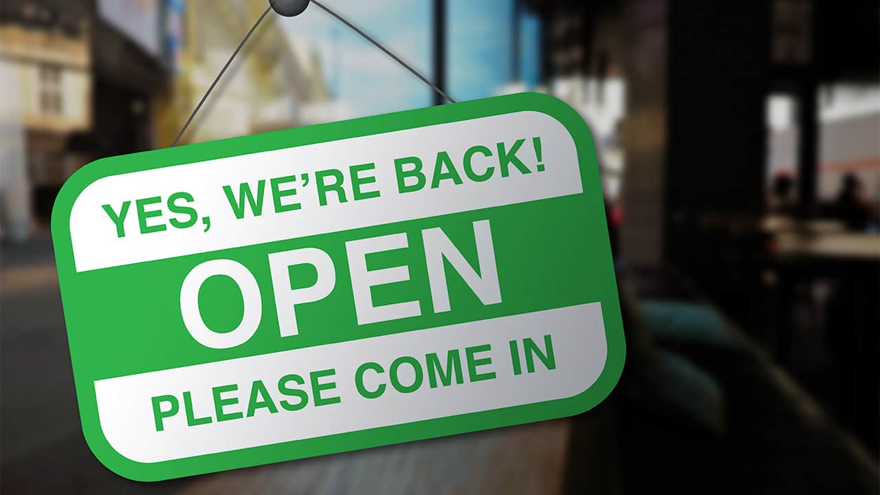 Photo of a sign on a business door welcoming customers back