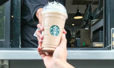 Image of a Starbucks employee handing a frappe mocha latte to a customer at drive thru counter.