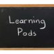 The words "Learning Pods" written in white chalk on a blackboard